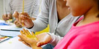 Dziewczynka w przedszkolu maluje farbami swoją dłoń