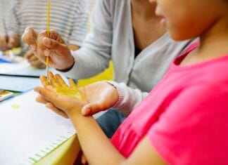 Dziewczynka w przedszkolu maluje farbami swoją dłoń
