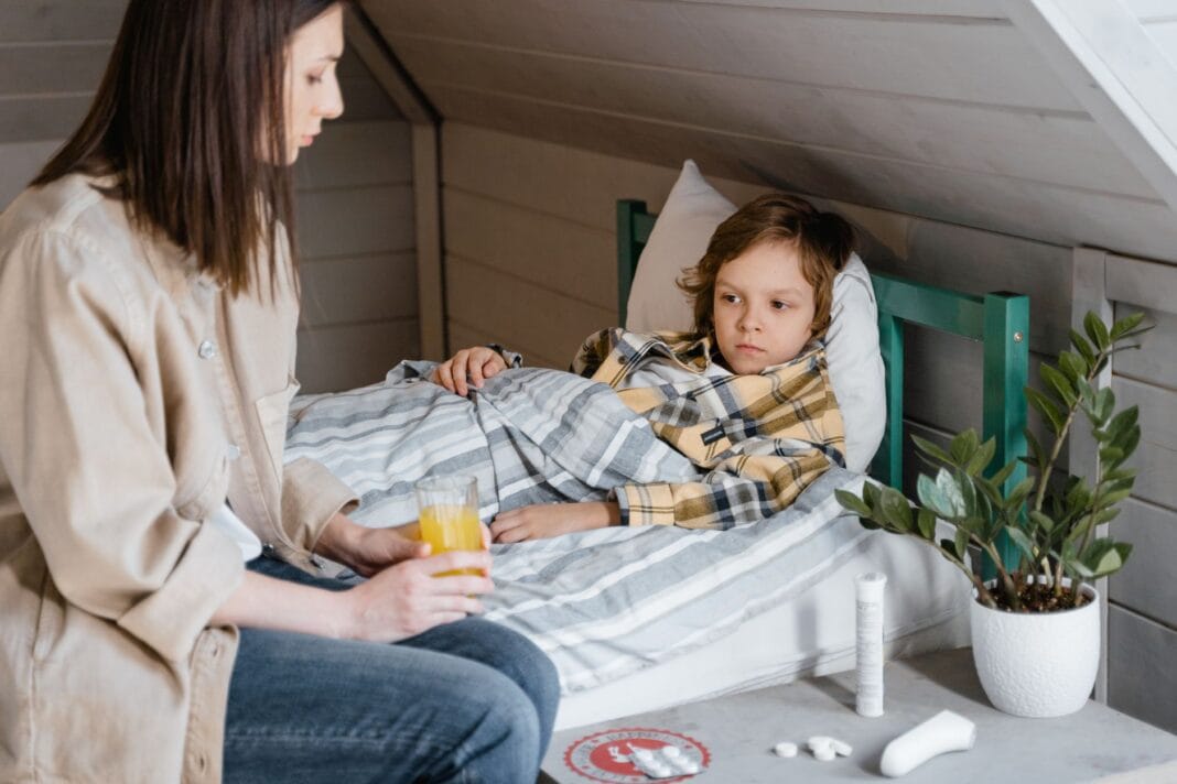 Mama podaje sok pomarańczowy choremu dziecku leżącemu w łóżku Mama podaje sok pomarańczowy choremu dziecku leżącemu w łóżku