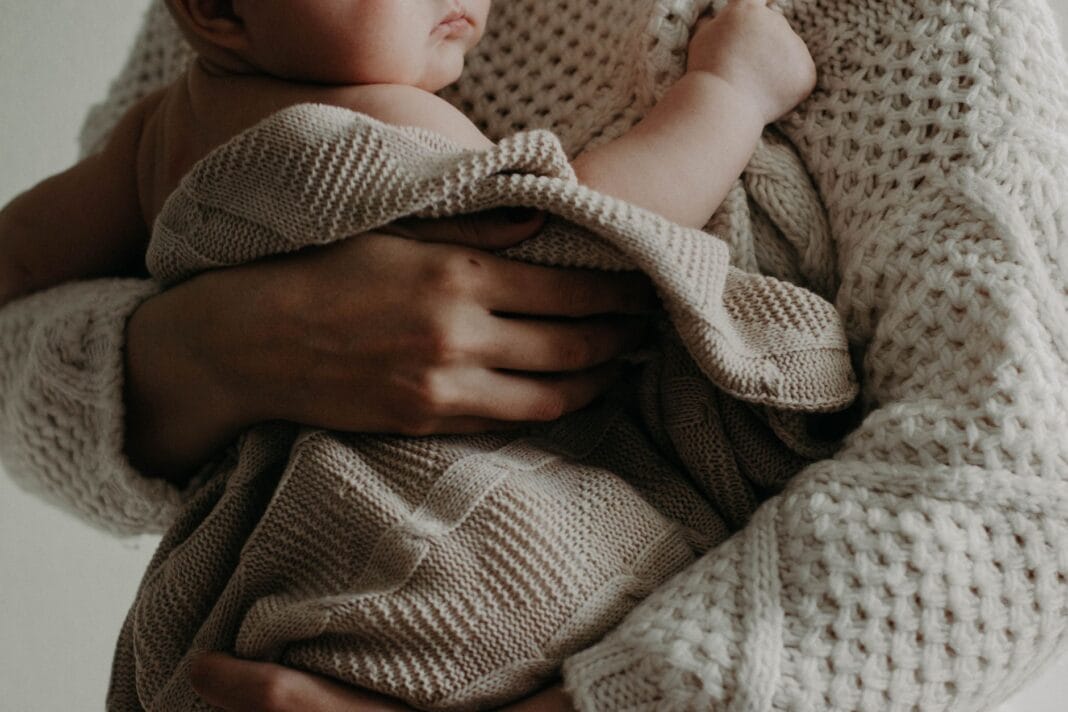 Mama tuląca niemowlę owinięte kocykiem w ciepłym uścisku Mama tuląca niemowlę owinięte kocykiem w ciepłym uścisku