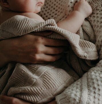 Mama tuląca niemowlę owinięte kocykiem w ciepłym uścisku