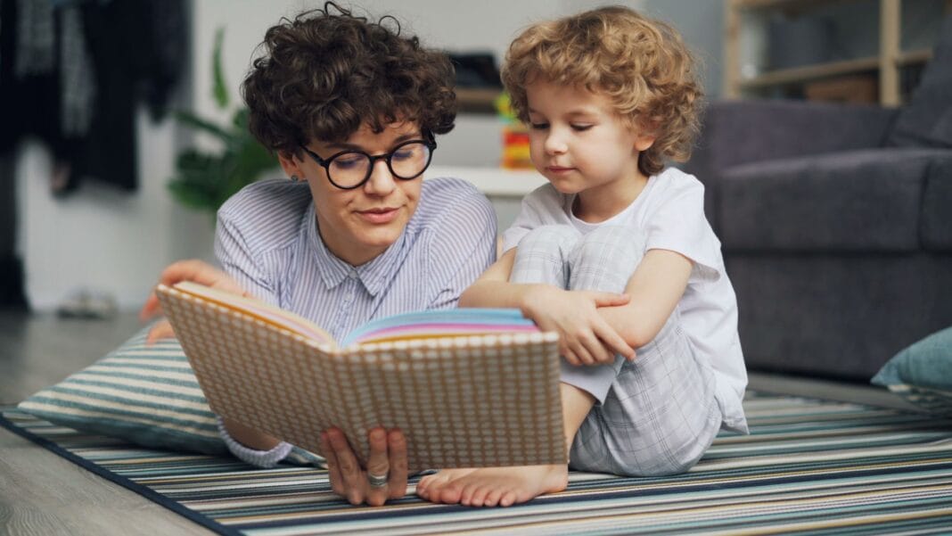 Mama z małym synem czytają razem książkę na dywanie Mama z małym synem czytają razem książkę na dywanie